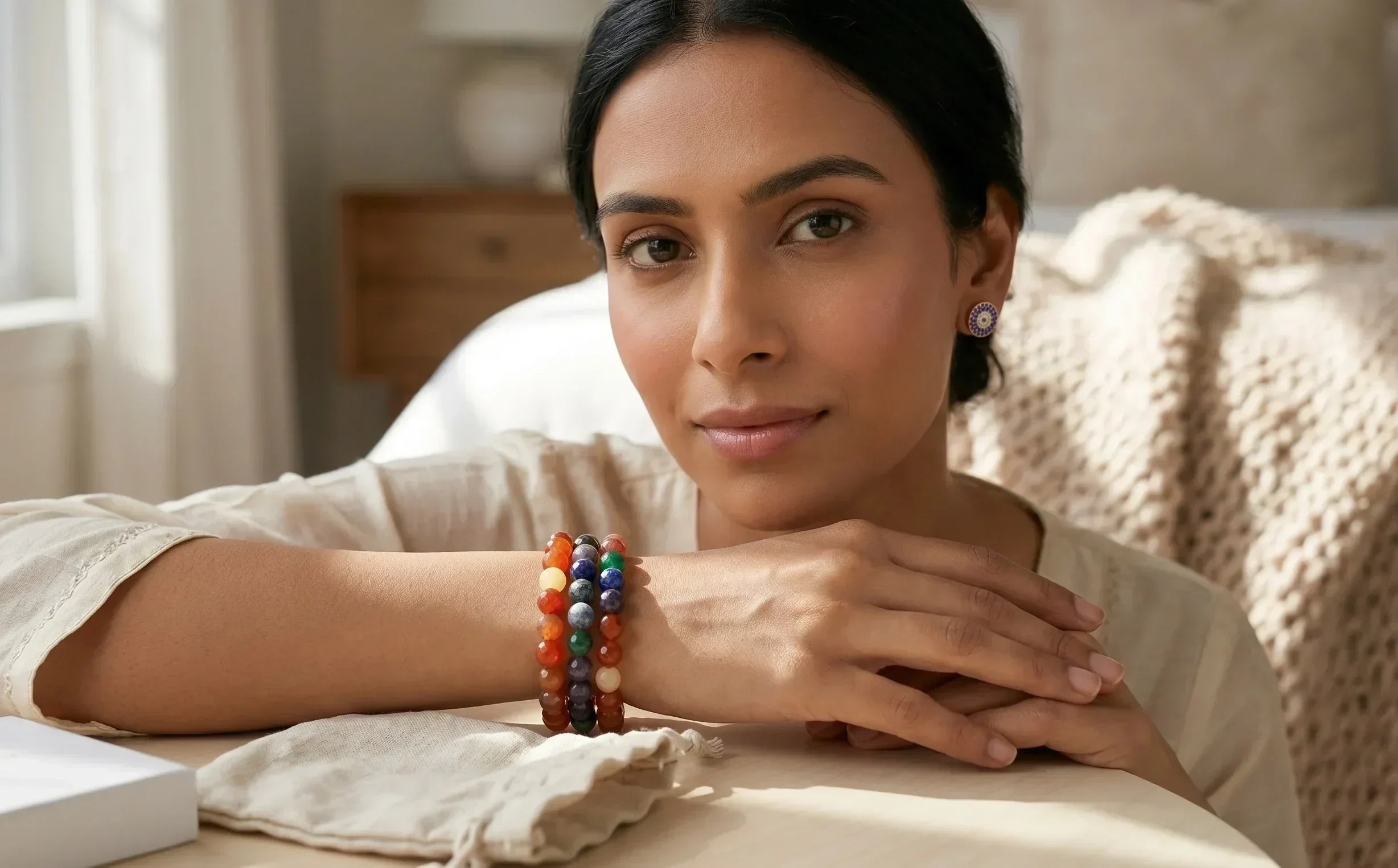 Woman sitting on a couch with colorful bracelets on her wrist, in a cozy indoor setting.