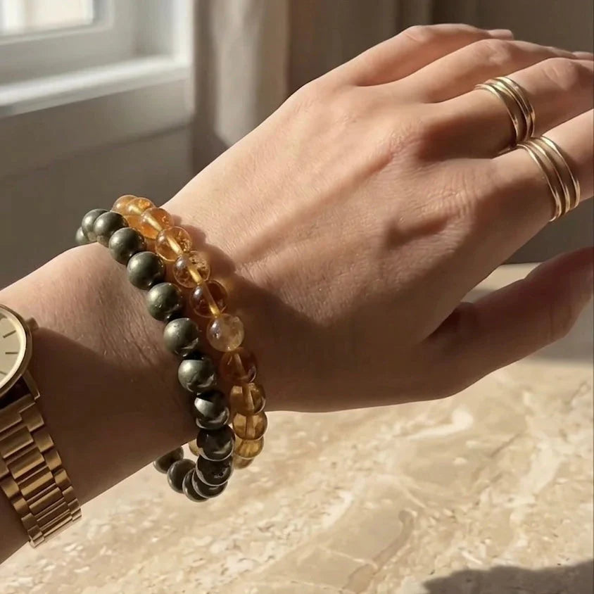 Hand wearing multiple bracelets pf pyrite and citrine and rings on a neutral background