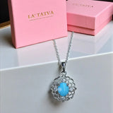 Turquoise pendant necklace with silver chain on a white surface, against a pink 'LA' TATVA' box.
