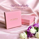 Two pink LA TATVA gift boxes on a soft satin fabric background with white and purple flowers for a thoughtful gift.