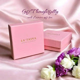 Two pink LA TATVA gift boxes on a soft satin fabric background with white and purple flowers for a thoughtful gift.
