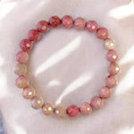 LA TATVA natural pink rhodonite gemstone stretch bracelet with faceted beads on a soft, light-toned fabric background.