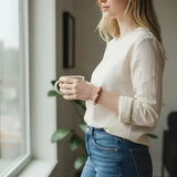 A woman wearing a LA TATVA natural pink Rhodonite gemstone bead stretch bracelet while holding a mug by a window.