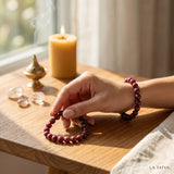 LA TATVA ruby beaded bracelet stack on a woman's wrist, featuring natural red gemstones on a wooden table with candle.