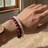 LA TATVA handcrafted ruby and pearl beaded bracelet stack worn on a wrist with a gold watch and rings.